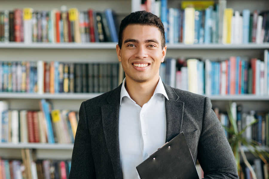 hispanic man smiling in front of library book shelves