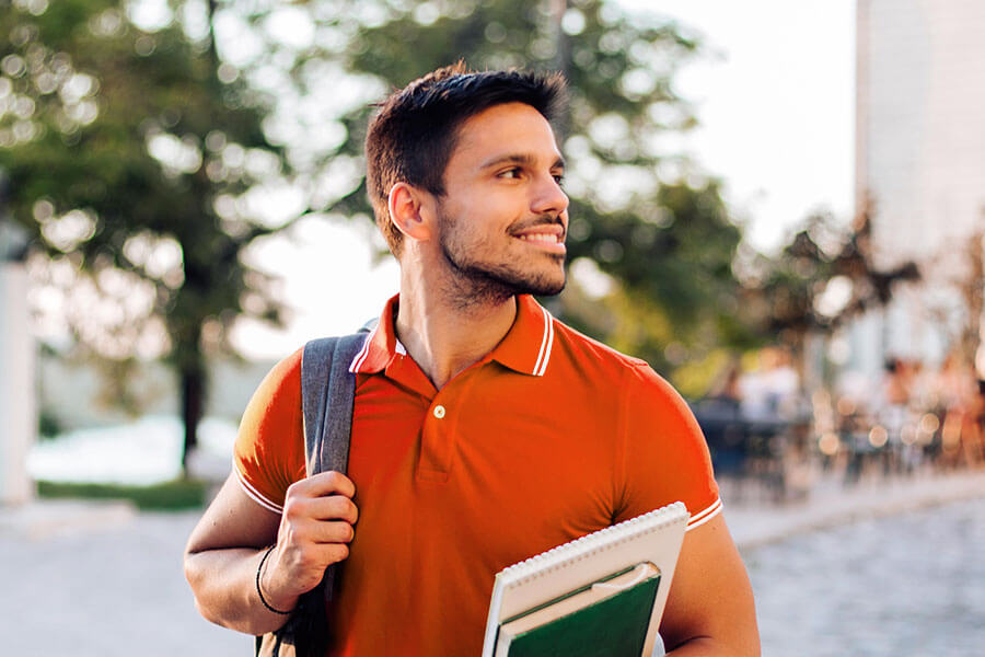 hispanic man smiling and holding books outdoors